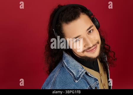 Ein bärtiger junger Mann lächelt warm, während er in einer gemütlichen Innenumgebung Musik hört. Stockfoto