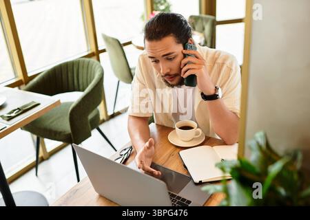 In einem schicken Café arbeitet ein junger Mann mit Bart ferngesteuert an seinem Laptop und konzentriert sich auf einen Anruf. Stockfoto