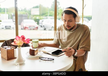 Ein bärtiger junger Mann sitzt in einem Café, schlürft Matcha und schreibt Notizen Stockfoto