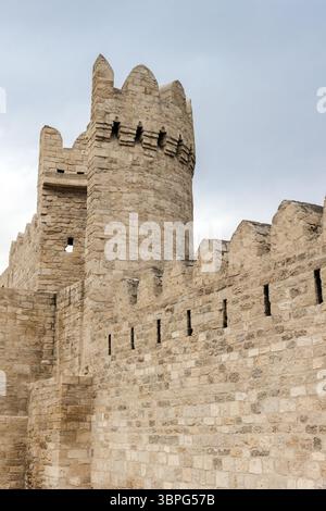 Alte Steinfestungsmauern mit einem strukturierten runden Turm unter einem blauen bewölkten Himmel, der beispielhaft für historische Architektur und mittelalterliche Verteidigungsarchitektur ist Stockfoto