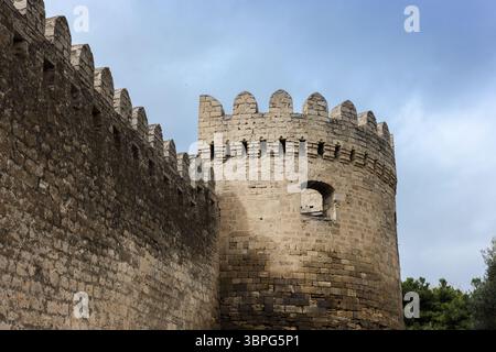 Alte Steinfestungsmauern mit einem strukturierten runden Turm unter blauem Himmel mit hellen Wolken, ein Beispiel für historische Architektur und mittelalterliche Defe Stockfoto