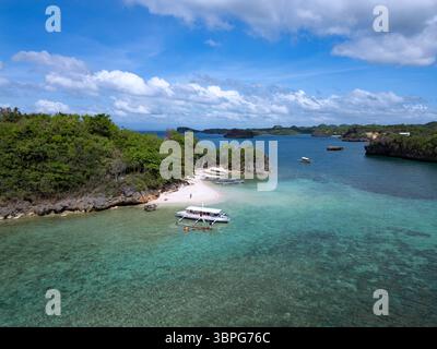 Blick aus der Vogelperspektive auf das türkisfarbene Wasser trifft auf den weißen Sandstrand am Natago Beach, gesäumt von grünen Bäumen unter hellem Himmel, Guimaras, Western Visayas, Philippinen. Stockfoto