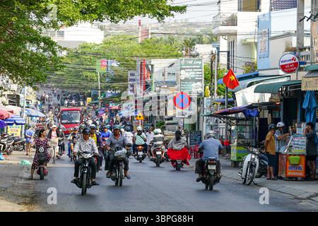 Mui ne, Vietnam, 22. März 2025: Eine belebte Straße voller Motorräder, lokaler Händler, Geschäfte, Schilder und der Energie des Alltags unter klarem Himmel Stockfoto