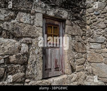 Alte, abgenutzte Tür und ein typisches gelb gerahmtes Fenster, das in eine Steinmauer einer Wohnung in Sistelo, Portugal, eingebaut ist. Stockfoto