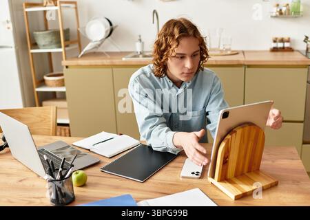 Ein junger Mann an einem gemütlichen Küchentisch, eingetaucht in Kreativität auf seinem Tablet. Stockfoto