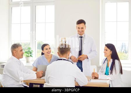 Gruppe glücklicher Ärzte in einer Klinik, die zusammen an einem Tisch sitzen, Nahaufnahme Stockfoto