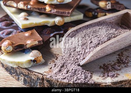 Kakao auf Holzlöffel und Schokoladentafeln mit Haselnüssen auf rustikalem Rundbrett. Warmes und Gourmet-Image, Seitenlicht, Stockfoto