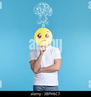 Mann, der sein Gesicht mit denkendem Emoticon auf hellblauem Hintergrund bedeckt. Verwirrte Gedanken als Explosion über seinem Kopf. Stress, Angst, Depression Stockfoto