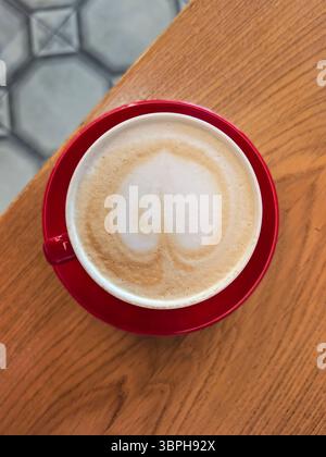 Cappuccino mit Herz Latte Art in Red Cup auf dem Tisch Stockfoto