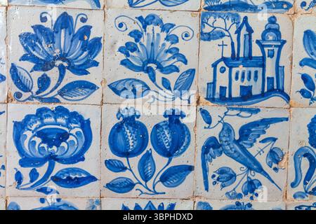 Eine detaillierte Nahaufnahme einer Wand, die mit traditionellen portugiesischen blauen und weißen Azulejo-Fliesen bedeckt ist, zeigt ein sich wiederholendes Muster verschiedener Motive einschließlich Stockfoto