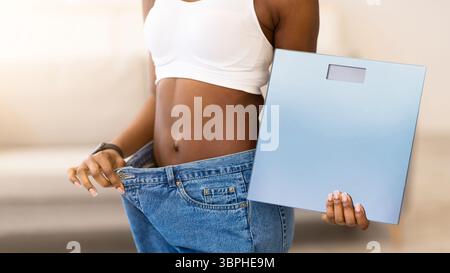 Slim Woman Holding Waagen Tragen Große Jeans Nach Dem Slimming Indoors Stockfoto