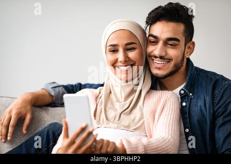 Glücklich erwartet muslimischen Paar Selfie auf dem Smartphone beim Entspannen Zu Hause Stockfoto
