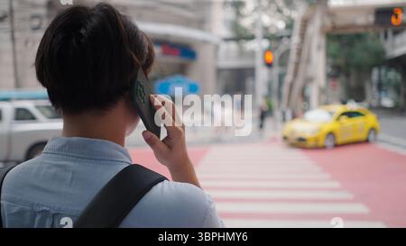 Geschäftsmann, der auf dem Smartphone steht, während er auf der Stadtstraße steht, mit Taxi und Fußgängerübergang im Hintergrund Stockfoto