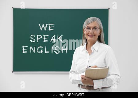 Lehrer in der Nähe der grünen Tafel mit Text Wir sprechen Englisch. Sprachkurs Stockfoto