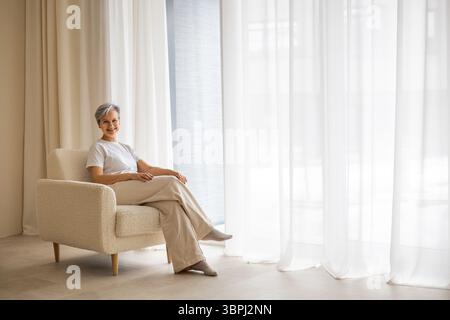Eine ältere, reife, schöne, gepflegte Rentnerin sitzt am Fenster Stockfoto