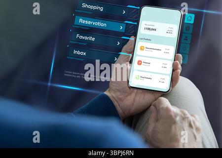 Eine Nahaufnahme von hinten eines Mannes in entspannter Haltung, der ein Mobiltelefon hält, mit einem Online-Anwendungsbildschirm, der eine futuristische Benutzerinterfa zeigt Stockfoto