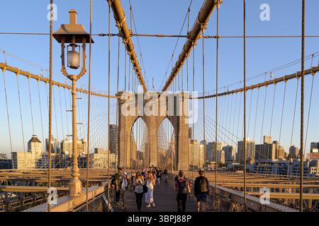 Fußgänger überqueren die Brooklyn Bridge während der goldenen Stunde mit der Skyline von Brooklyn im Hintergrund, New York City, USA. Stockfoto