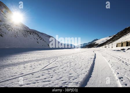 Die Sonne blickt hinter einer Bergmauer in einem verschneiten Hochtal in den Schweizer Bergen, Andermatt, Schweiz, Europa Stockfoto