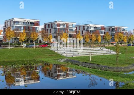 Moderne, quaderförmige Wohnhäuser spiegeln sich in einem Rücklaufbecken für Regenwasser bei wolkenlosem Himmel und sonnigem Wetter in Frankfurt am Main wider Stockfoto