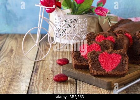 Valentinstag, Geburtstag oder Muttertag Dessert, hausgemachte festliche Speisen. Hausgemachter süßer Schokoladen-Brownie-Kuchen mit rotem Herz auf einem rustikalen Holzboden Stockfoto