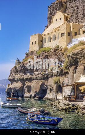 Ein in den Felsen der Klippe im Krater der Insel San Turin im östlichen Mittelmeer gebautes Haus mit verschiedenen Ruderbooten und Motorbooten anc Stockfoto