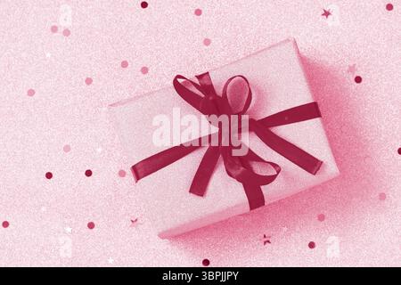 Trendige Farbe des Jahres 2023 - Viva Magenta. Handgemachte Weihnachtsgeschenkbox auf goldenem Hintergrund. Weihnachten präsentiert goldene Box mit rotem Band Stockfoto