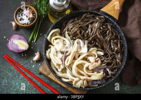Scharfe Nudeln, traditionelles koreanisches Essen. Buchweizen-Soba-Nudeln und Tintenfisch mit Sauerrahmsauce auf einem dunklen Steintisch Stockfoto