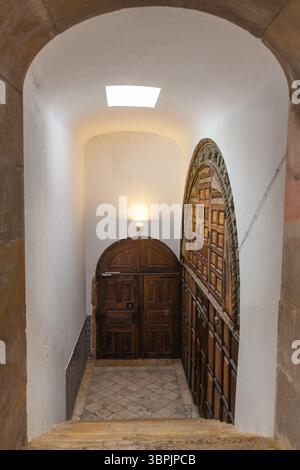 Ein historischer Bogengang führt zu einer aufwändig geschnitzten Holztür und einer großen dekorativen Holzwand, die von warmem künstlichem Licht beleuchtet wird Stockfoto