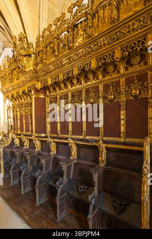 Ein großartiges Interieur mit kunstvollen Holzbänken mit satten roten Polstern, komplizierten goldenen Schnitzereien und heraldischen Schildern, die auf einem Steinbogenrücken platziert sind Stockfoto