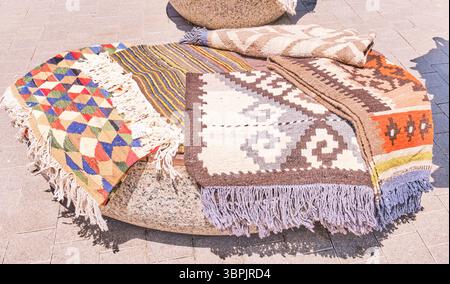 Kasachstan, Almaty - 28. Juni 2025: Farbenfrohe handgewebte Teppiche mit traditionellen kasachischen Ornamenten, die während eines lokalen Handirs im Freien auf einer Steinbank ausgestellt wurden Stockfoto