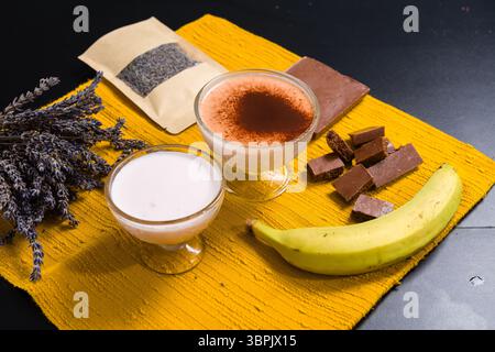 Zwei Desserttassen, Schokolade, Banane und Lavendel auf einer gelben Matte. Stockfoto