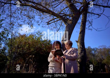 Eine Frau mittleren Alters und eine ältere Mutter mit heiliger Bibel in Händen betend für Frieden im Herbstwald Stockfoto