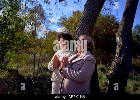 Eine Frau mittleren Alters und eine ältere Mutter mit heiliger Bibel in Händen betend für Frieden im Herbstwald Stockfoto