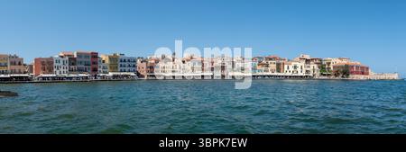 Chania, Kreta, Griechenland - 22. Juni 2025: Lebendige Gebäude spiegeln sich im Wasser, während die Menschen Cafés entlang des Hafens in Chania genießen. Stockfoto