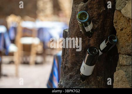 Chania, Kreta, Griechenland - 22. Juni 2025: In einer charmanten Taverne in Chania werden Weinflaschen kreativ an einer Steinmauer angeordnet. Stockfoto