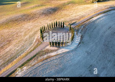 Aus der Vogelperspektive eines faszinierenden Kreises aus schlanken Zypressen, die lange Schatten auf den sanften Hügeln der Toskana werfen, San Quirico d'Orcia, Toscana, Italien. Stockfoto