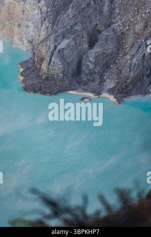 Blick auf das türkisfarbene Wasser trifft auf den zerklüfteten, dunklen vulkanischen Felsen in einem faszinierenden Tanz aus Farbe und Textur, Ijen Vulkankrater, Ost-Java, Indonesien. Stockfoto