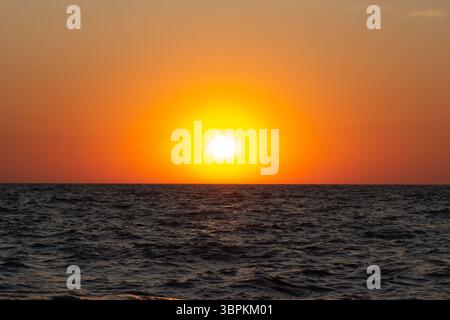 Ein lebhafter Sonnenuntergang über dem Meer mit warmen Farben, die sich auf den sanften Wellen spiegeln Stockfoto