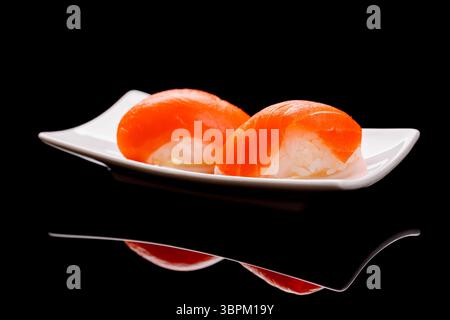 Lachsushi auf einem Teller mit frischen Zutaten und lebhaften Farben auf einem sauberen schwarzen Hintergrund Stockfoto