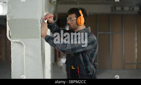Mann Bauingenieur Reparaturmann mit Maßband auf der Baustelle Gebäude überprüfen Wandmaße Wohnung Renovierung männlicher Vorarbeiter Stockfoto