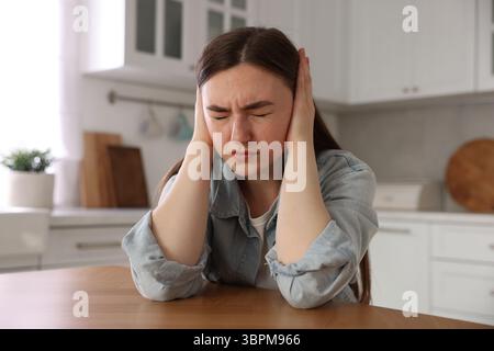 Verängstigte Frau, die an Paranoia am Holztisch in der Küche leidet Stockfoto
