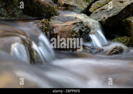Der schnelle Gebirgsbach fließt über den felsigen Boden und bildet Kaskaden, clearwater Murmeln über Steine und moosbedeckte Felsen Stockfoto