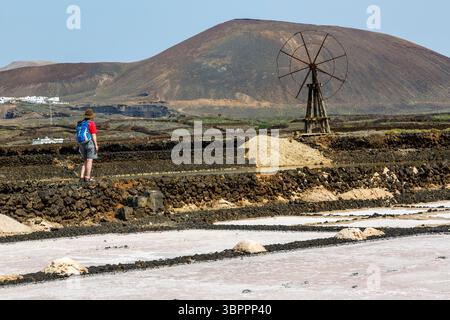 Person, die auf Salinen steht und Überreste der Pumpwindmühle, Salinas de los Agujeros, Los Cocoteros, Lanzarote, Kanarische Inseln, Spanien Stockfoto