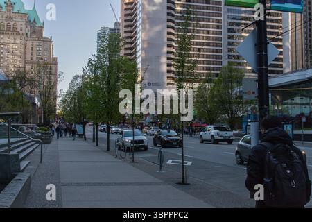 Vancouver, KANADA - 19. April 2024 : urbane Szene in der Innenstadt von Vancouver mit Verkehr, Fußgängern und grünen Bäumen, die an einem klaren Abend den Bürgersteig säumen. Stockfoto