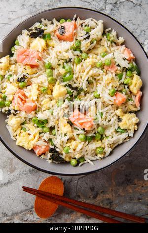 Gebratener Reis mit Gemüse, Lachs, Ei und Algen in der Schüssel auf dem Tisch. Vertikale Draufsicht von oben Stockfoto
