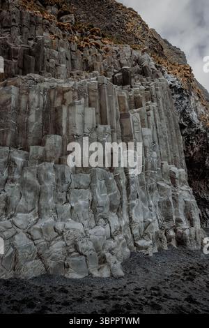 Panoramablick auf den schwarzen Sandstrand von Reynisfjara mit Basaltsäulen und Wellen unter bewölktem Himmel Stockfoto