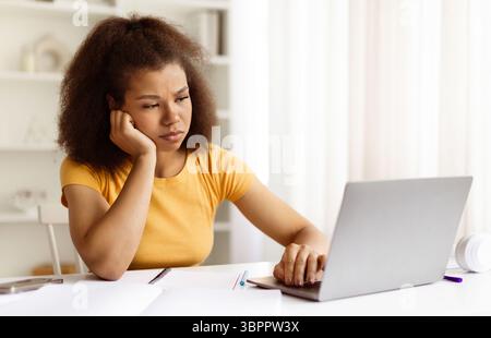 Frustrierte schwarze Frau, die auf einen Laptop blickt und sich bei der Arbeit von zu Hause aus gestresst fühlt Stockfoto