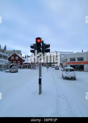 Eine verschneite Stadtstraße mit einer einzigartigen Ampel mit einem herzförmigen roten Signal. Die Szene weckt Gefühle von Liebe, Wärme und Fürsorge inmitten des C Stockfoto