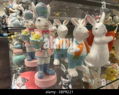 Eine Sammlung von keramischen Osterhasen mit Karotten und Küken, ausgestellt auf Glasregalen in einem Geschäft. Geeignet für Einzelhandel, Urlaub Stockfoto