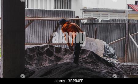 Ein Bauarbeiter, der Sand vor Ort manuell hackt, zeigt Entschlossenheit, körperliche Arbeit und Beharrlichkeit bei der Vorbereitung der Bodenarbeiten. Stockfoto